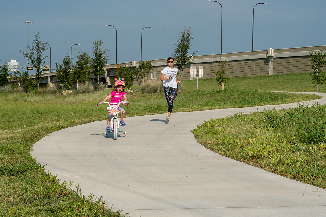 Woman running and little girl biking on 290 Trail
